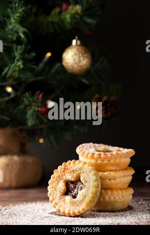 Vier, hausgemachte Weihnachtskuchen auf einer Tischplatte. Die Torten werden in einer weihnachtlichen Umgebung mit einem geschmückten Baum im Hintergrund gesetzt Stockfoto