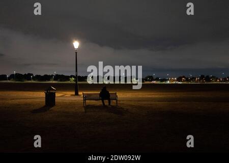 Eine Person sitzt auf einer Bank auf Blackheath in der Nacht Stockfoto