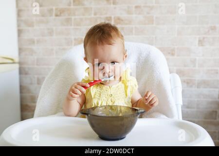 Glückliches Baby, das im Hochstuhl sitzt und griechischen Joghurt isst. Stockfoto