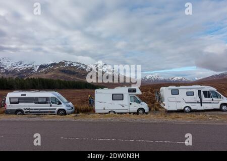 Drei Wohnmobile in einer Reihe an der Seite geparkt Eine Hauptstraße mit schottischen schneebedeckten Bergen in der Hintergrund Stockfoto