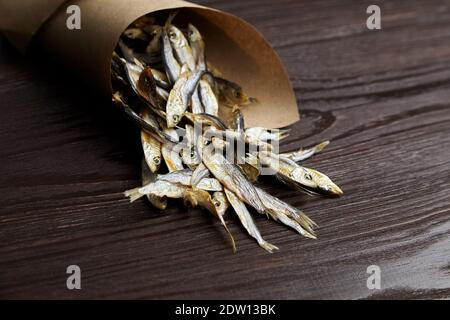 Sonnengetrockneter salziger kleiner Fisch. Stockfisch in Papiertüte auf dunklem Holzhintergrund. Stockfoto