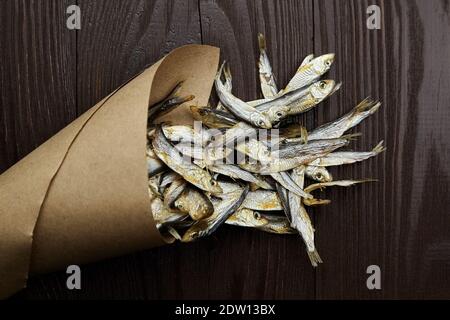 Sonnengetrockneter salziger kleiner Fisch. Stockfisch in Papiertüte auf dunklem Holzhintergrund. Stockfoto