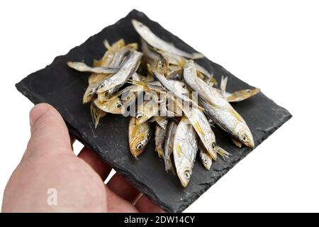 Kleine getrocknete Fische auf schwarzem Schieferbrett in einer Hand Isoliert auf weißem Hintergrund Stockfoto