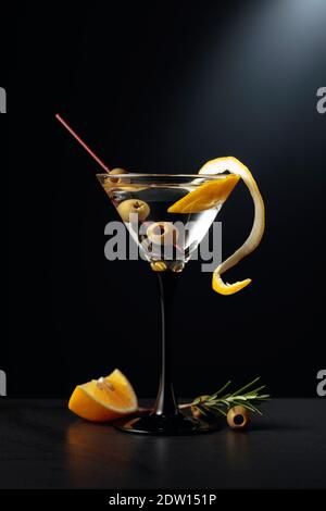 Trockener martini mit Zitronenschale und grünen Oliven auf schwarzem Hintergrund. Stockfoto