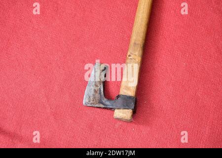 Eine Axt bleibt auf rotem Teppich. Schneideseite und Griff aus Metall aus Holz. Auf der metallischen Seite ist Korrosion zu sehen. Stockfoto