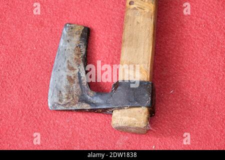 Eine Axt bleibt auf rotem Teppich. Schneideseite und Griff aus Metall aus Holz. Auf der metallischen Seite ist Korrosion zu sehen. Stockfoto