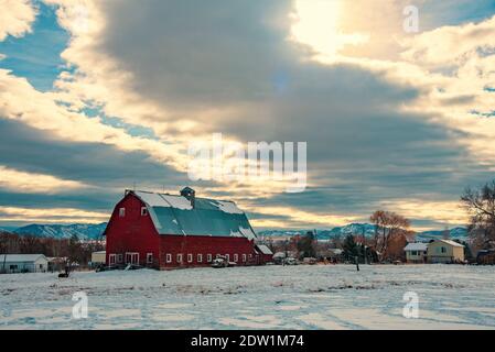 Vintage, rote Milchscheune in einem Schneefeld. Das Aufräumen von Sturmwolken sorgt für Dramatik und Klarheit in der ländlichen Szene. Stockfoto