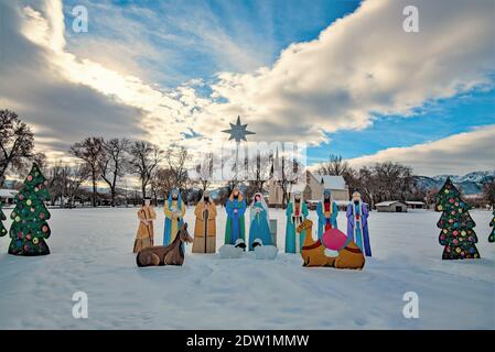 Wellsville, Utah, USA, 21. Dezember 2020. Hausgemachte Krippe zusammen mit weltlichen Dekorationen. Eine alte LDS Kirche im Hintergrund. Stockfoto