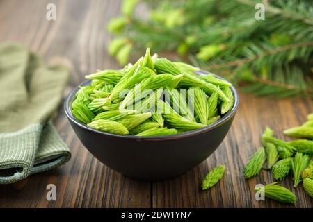 Fichtenspitzen in einer schwarzen Schale. Tannenknospen und Nadeln, Tannenzweige auf Holztisch. Stockfoto