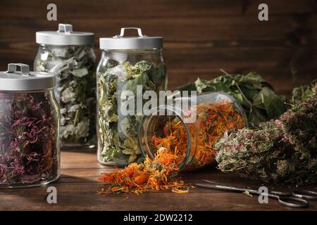Gläser mit trockenen Heilkräutern - Ringelblume, Koneblümchen, Himbeerblätter und Lindenbaumblumen, Heidekraut auf Holztisch. Alternative Me Stockfoto