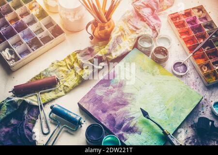 Künstlerische Ausrüstung - Leinwand und Palette Messer, Pinsel, bunte Farben im Künstlerstudio. Draufsicht. Stockfoto