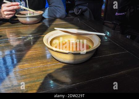 Eine Schüssel heiße Brühe, Rind oder Huhn, in einem kleinen chinesischen Restaurant in der Landschaft von Shanghai. Essstäbchen werden über den Behälter gelegt. Das Licht macht Stockfoto