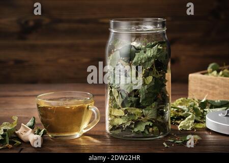 Tasse gesunder Tee mit Lindenblüten, Krug mit trockenen Blumen und Blätter von Linde oder Tilia cordata Baum. Behandlung von Erkältung und Grippe. Stockfoto