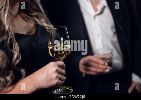 Ein blondes Mädchen in einem schwarzen Kleid mit einem Glas Champagner, ein Mann in einer Jacke mit einem Glas Whiskey, Nahaufnahme. Stockfoto