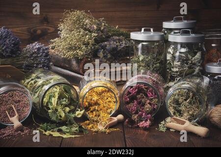 Gefäße mit trockenen Heilkräutern - Heidekraut, Ringelblume, Koneblüten, Lindenblüten, melisse, Bündel von trockenen Pflanzen, alte Bücher auf Holztisch. Alternative Stockfoto