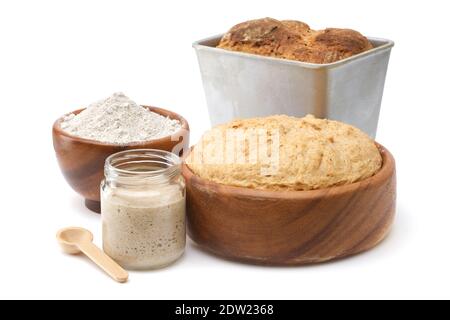NaturSauerteig für Brot im Glasgefäß, Holzschüssel mit Teig, Schüssel mit Mehl und frisch gebackenem Brot in Backform auf weiß. Stockfoto