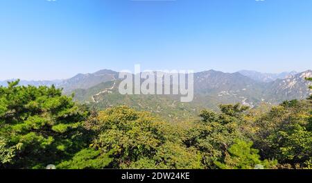 Panoramablick von der majestätischen Chinesischen Mauer auf die umliegende Landschaft und Wälder. Der Horizont ist im blauen Dunst. Bäume vor dem Hotel Stockfoto