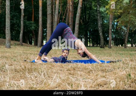 Sicheres Fitnessstudio oder Fitnesscenter im Freien. Familie durch gemeinsames Training in Parks fit bleiben. Mutter praktiziert Yoga mit ihrem Baby Tottdler Tochter in der Stockfoto