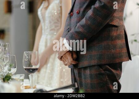 Gesichtslose Braut und Bräutigam stehen neben dem Hochzeitstisch mit gekreuzten Händen. Brautpaar im Restaurant. Hochzeitsfeier Stockfoto