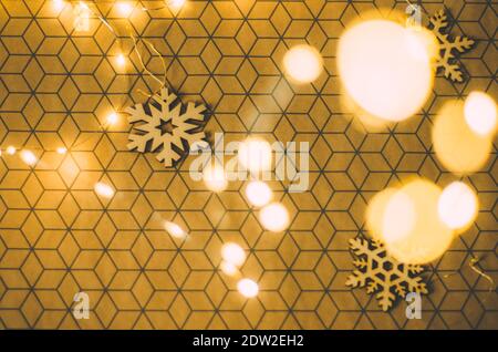 Goldenes Bokeh weihnachtsbeleuchtung auf einem 3d gemusterten Geschenkpapier Mit hölzernen Schneeflocken Dekorationen Stockfoto
