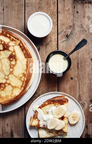 Dünne Pfannkuchen, Crepes mit Bananen und Kondensmilch auf einem Teller auf einem Holztisch. Stockfoto