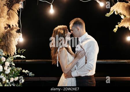 Braut und Bräutigam umarmen sich vor dem Hochzeitstor mit Licht. Hochzeitsfeier. Glückliches Brautpaar am Ende der Hochzeit Stockfoto