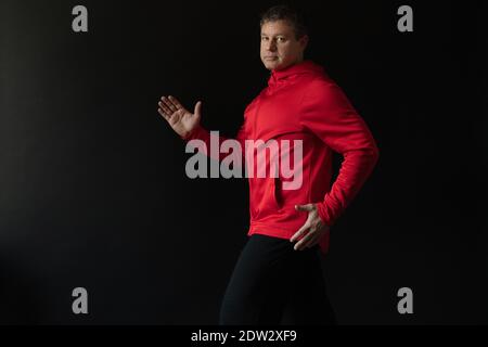 Porträt eines nachdenklichen männlichen Athleten im Alter von 35 bis 45 Jahren in rotem Sportkleid auf schwarzem Hintergrund. Stockfoto
