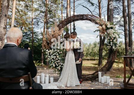Mann, der bei der Hochzeitszeremonie ein Bild vom küssenden Bräutigam und der Braut gemacht hat. Glückliches Jungvermählte bei der Hochzeitszeremonie Stockfoto
