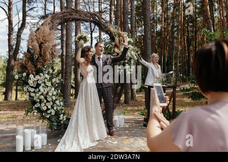 Glückliche Braut und Bräutigam, nachdem sie sich VOR dem Hochzeitstor GEGENSEITIG JA gesagt haben. Frisch verheiratetes Paar bei der Hochzeitszeremonie draußen Stockfoto