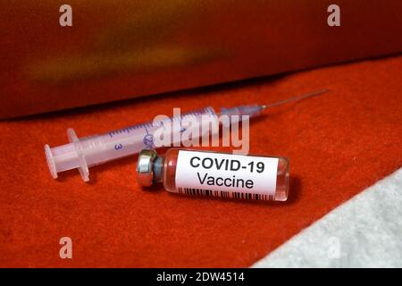 COVID-19 Impfstoffflasche und Spritze auf rotem Weihnachtsmütze für Weihnachtsfeierlichkeiten während der Coronavirus-Pandemie. Konzept der Wintersaison, Gesundheit, Stockfoto