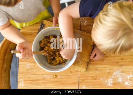 Kinder, die zu Hause auf einem Küchentisch essen Mischen Plätzchenteig Stockfoto