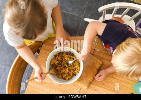 Kinder, die zu Hause auf einem Küchentisch essen Mischen Plätzchenteig Stockfoto