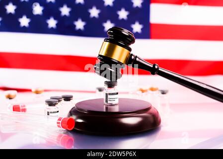 Gerichtliche Gavel auf den Apotheken, die Coronavirus-Impfstoff verkaufen, mit einem unfokussierten amerikanischen Flagge Hintergrund. Stockfoto