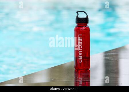 Rettungsschwimmer Trinkflasche neben hellblauem Pool. Stockfoto