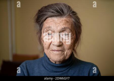 Ältere kaukasische ältere Großmutter neunzig Jahre alt schaut aufmerksam und lächelt, fühlt sich glücklich, großes Porträt, Gesicht mit tiefen Falten, graue Haare. T Stockfoto