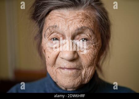 Ältere niedliche Frau von neunzig Jahre alt Kaukasisch mit grauen Haaren und faltigen Gesicht sieht in der Kamera, nette Art Look und lächelt.Reife Großmutter im Ruhestand Stockfoto