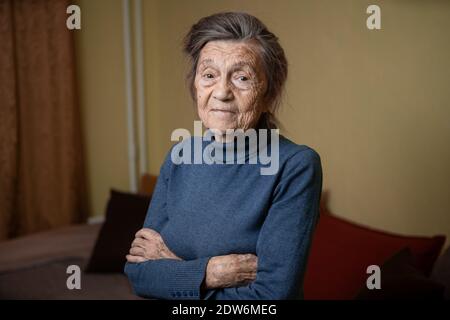 Ältere kaukasische ältere Großmutter neunzig Jahre alt schaut aufmerksam und lächelt, fühlt sich glücklich, großes Porträt, Gesicht mit tiefen Falten, graue Haare. T Stockfoto