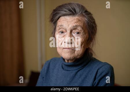 Ältere kaukasische ältere Großmutter neunzig Jahre alt schaut aufmerksam und lächelt, fühlt sich glücklich, großes Porträt, Gesicht mit tiefen Falten, graue Haare. T Stockfoto