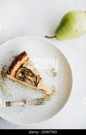 Flaches Stück vegan milchfrei zuckerfreier Birnenkäsekuchen in rustikalem Teller und frischer Birne auf weißem Marmortisch-Hintergrund, Draufsicht. Modern V Stockfoto