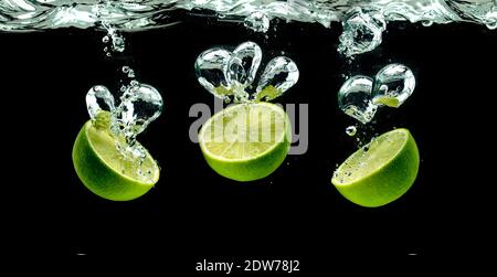 Bündel von Limettenfrüchten Hälften spritzt mit Blasen in Wasser Isoliert vor schwarzem Hintergrund Stockfoto