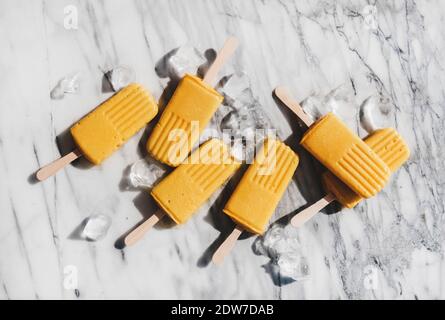 Mango Smoothie vegane Eis-Eis-Eiszapfen. Flache Mango-Fruchtpopsicles auf grauem Marmorboden unter Sonnenlicht, Draufsicht. Sommer gesund desse Stockfoto