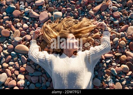 Eine Draufsicht auf ein blondes Haar Weibchen auf einem Stoned Strand posiert vor der Kamera Stockfoto