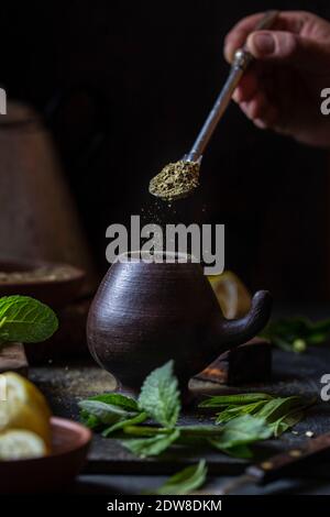 Lateinamerikanisches Heißgetränk Yerba Mate in Tonbecher, Kräuter und Zitrone. Stockfoto