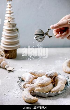 Hausgemachte traditionelle Weihnachten Mürbeteig Cookies Vanille Crescents mit Puderzucker bestreuen aus Sieb. Auf Keramikplatte mit hölzernen Weihnachtsdecorati Stockfoto