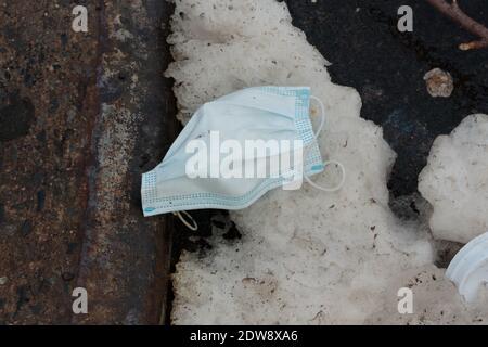 Eine weggeworfene Gesichtsmaske sät einen Straßenrand mit Schnee, als Symbol des Coronavirus oder der covid-19 Pandemie Stockfoto