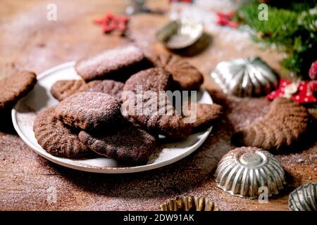 Hausgemachte traditionelle Weihnachten Mürbeteig Cookies Schokolade Crescents mit Kakao Puderzucker in Keramik-Platte mit Cookie-Formen, Tanne, rote Weihnachten st Stockfoto