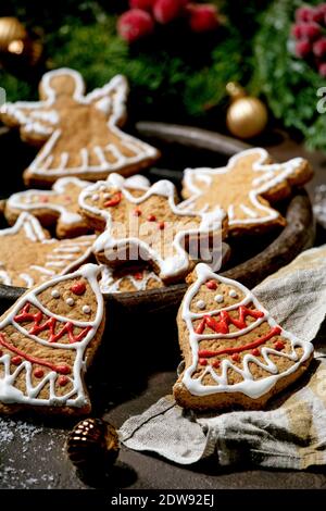 Hausgemachte traditionelle Weihnachten Lebkuchenkekse mit Verzierung verziert. Lebkuchenmann, Engel, Glocke auf Keramikplatte mit Weihnachtsdekorationen über dunklem BA Stockfoto