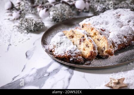 Traditionelle hausgemachte deutsche Weihnachten backen Stollenkuchen Brot auf Teller mit silbernen Weihnachtsdekorationen auf weißem Marmor Hintergrund. Stockfoto