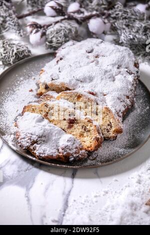 Traditionelle hausgemachte deutsche Weihnachten backen Stollenkuchen Brot auf Teller mit silbernen Weihnachtsdekorationen auf weißem Marmor Hintergrund. Stockfoto