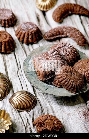Hausgemachte traditionelle Mürbeteig Kekse Schokolade Crescents mit Kakao Puderzucker in Keramik-Platte mit Plätzchen Formen über alten Holzhintergrund. Flach Stockfoto